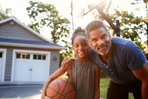 A man and girl holding a basketball in front of their home.