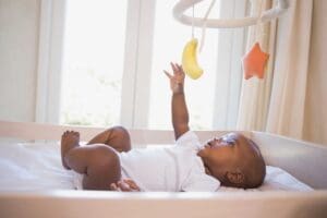 A baby is laying in the crib with his hands up.